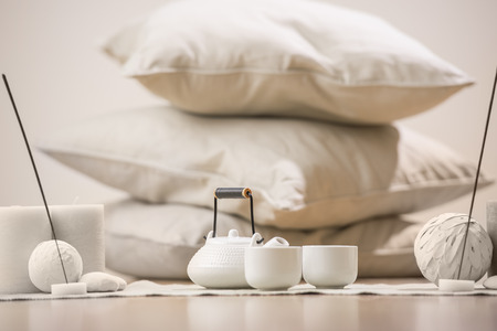 Teapot and cups with aromatic sticks and candles in front of pillows and decorations at homeの写真素材