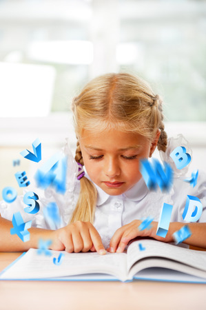 Portrait of a young girl in school at the desk. Reading book and dreaming. Graphic 3d symbols flying around herの写真素材