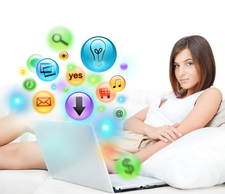 Portrait of pretty happy young woman sitting on couch with a laptop. Different icons appearing from the screenの写真素材