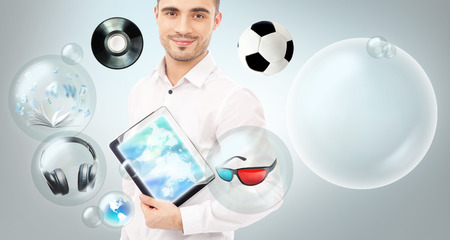 Adult handsome man holding tablet computer. Icons of different object are flying around. All multimedia in one mobile gadget conceptの写真素材