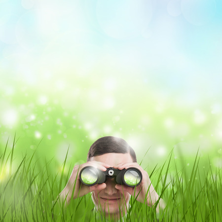 Man looking through binoculars from grass. Lots of copyspace. Head hunting or looking for something concept.の写真素材