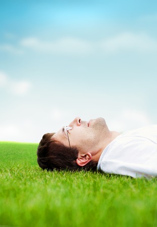 Young good looking man in white shirt lying on grass and looking at the skyの写真素材