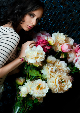 Portrait of young gorgeous woman with flowers at dark room with tile on wallsの写真素材