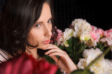 Portrait of young gorgeous woman with flowers at dark room with tile on wallsの写真素材