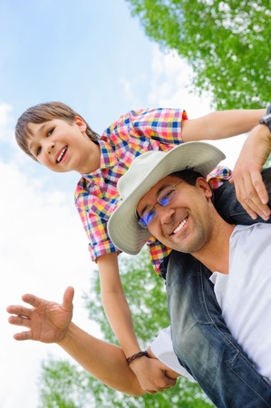 Portrait of smiling father giving his son piggyback ride outdoors against skyの写真素材