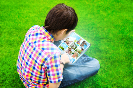 Little boy sitting on grass and using tablet computer to watch or share photo and video filesの写真素材