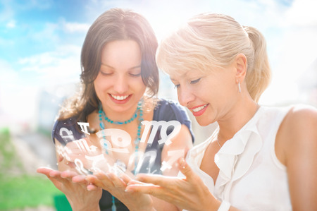 Two women mother and daughter sitting at summer park and having fun while discussing horoscope and different zodiac symbols appearing from their handsの写真素材