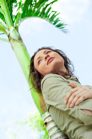 Portrait of young pretty woman leaning on palm tree and enjoying her freedom and sunの写真素材