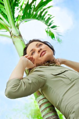 Portrait of young pretty woman leaning on palm tree and enjoying her freedom and sunの写真素材
