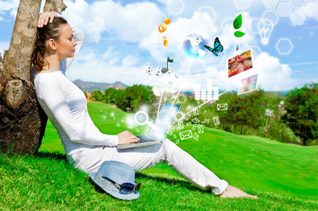 Pretty woman sitting by tree with laptop computerの写真素材
