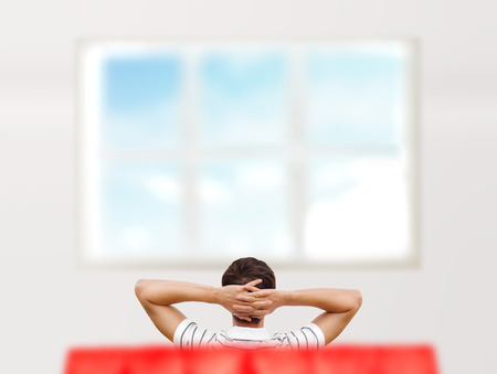 Young man sitting at his new home and looking at window. Photo from behindの写真素材