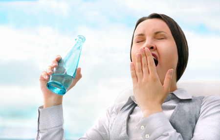 Portrait of beautiful business woman drinking water and yawning at officeの写真素材