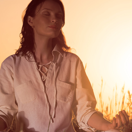 Beautiful Yoga woman siting against sunrise and rays of sun surrounding her. Retro style photoの写真素材