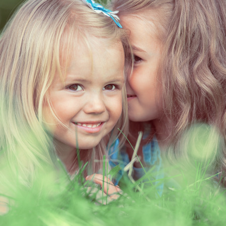 Happy children relaxing on grass in summer park and talking. Retro style photoの写真素材