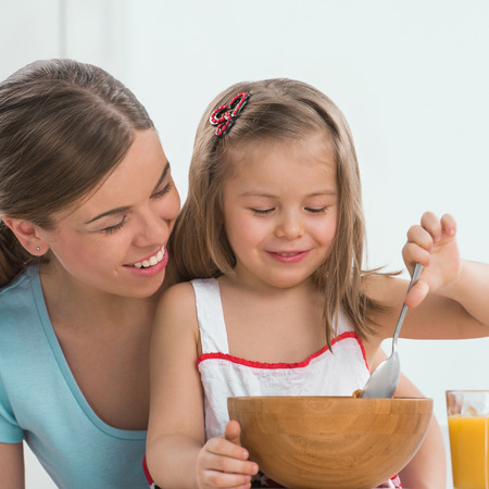 Portrait of adorable young girl and mother in a playful mood having breakfast at homeの写真素材