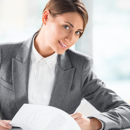 Front view of business woman looking over papers on clipboard at her officeの写真素材