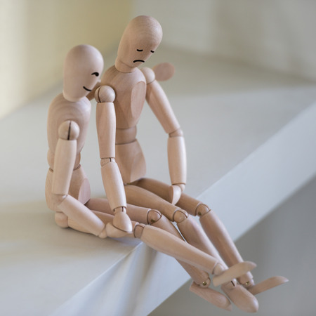 Wooden people sitting at home and supporting each other. People relationship concept. Drawn facesの写真素材