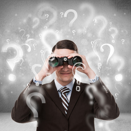 Handsome business man with binoculars and question marks above his headの写真素材