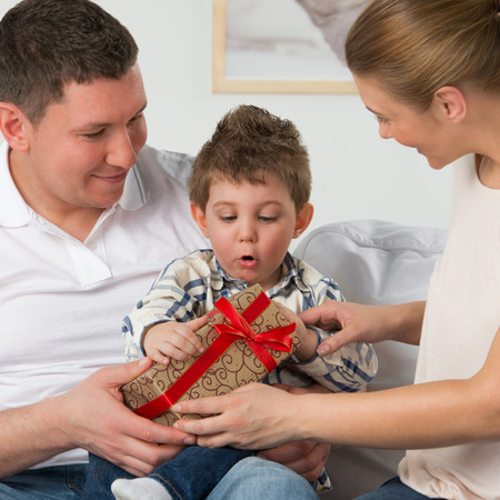 Couple giving gift to their little son in the living room. Happy family portraitの写真素材