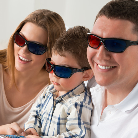 Family laughing while watching television together in the living-room wearing 3d glassesの写真素材