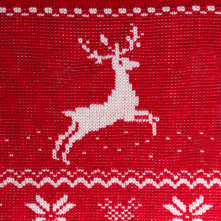Real red knitted background with white Christmas deers and snowflakesの写真素材