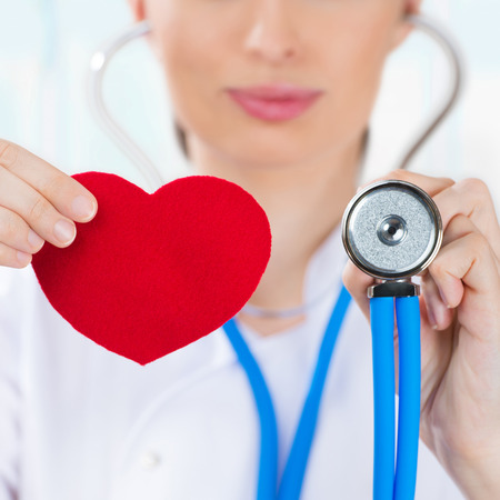Female doctor with stethoscope holding red human heart at hospitalの写真素材