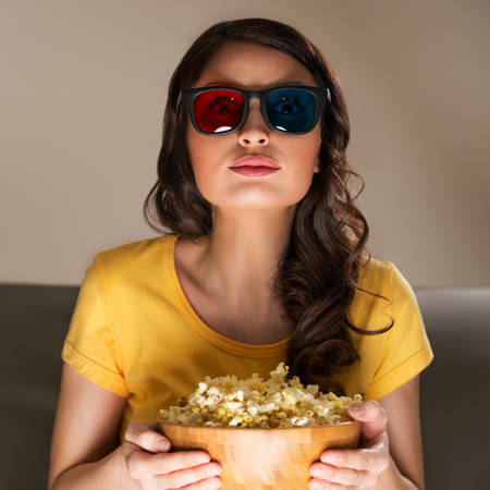 Young woman with popcorn and 3d glasses watching movie at homeの写真素材