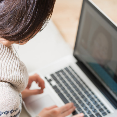 Portrait of a young woman with headphones, lying in front of her laptop and chatting with her grandmother, photo from behind, granny on the screenの写真素材