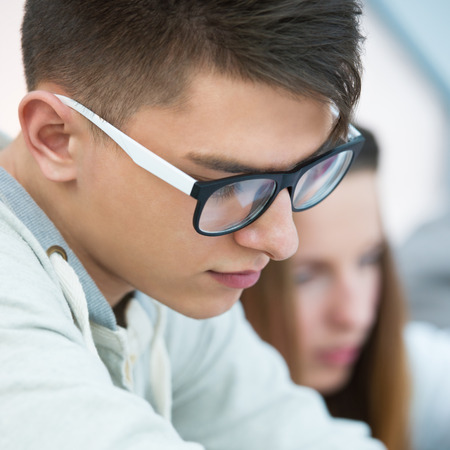 High School students. Young handsome man student sitting in classroom with his female classmate and making notes during lecture. の写真素材