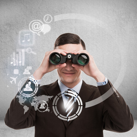 Technology concept. Businessman with biboculars and virtual interface with web and social media iconsの写真素材