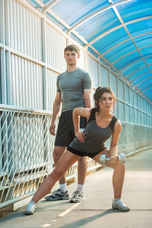 Athletic couple pumping up muscles with dumbbells outdoors in the cityの写真素材