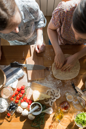 Two women cooking pizza at home. Filling pizza with ingredients. Top view. Overhead view.の写真素材
