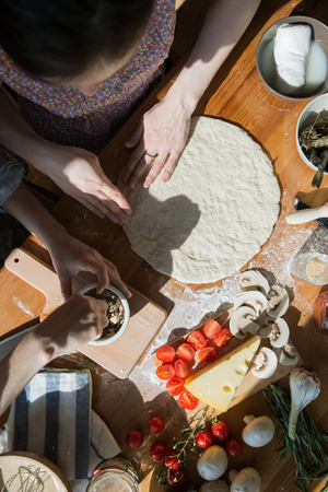 Two women cooking pizza at home. Filling pizza with ingredients. Top view. Overhead view.の写真素材