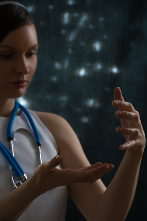 Pretty female doctor with stethoscope wearing futuristic clothes holding something in her handsの写真素材