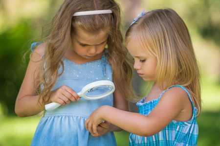 Children with a magnifying glass. Two little sisters of friends looking through magnifier at flowerの写真素材