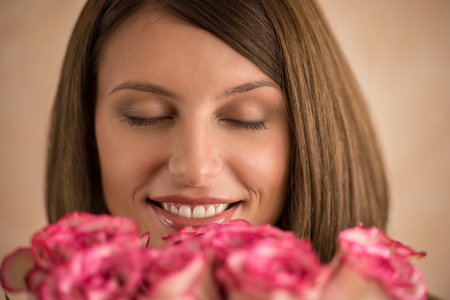 Beautiful woman with a large bouquet of flowers in her arms smelling a fragrant pink roseの写真素材