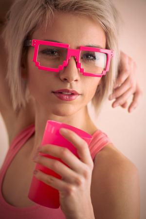 Hot blond girl with short hair wearing freak glasses holding plastic cup and looking at cameraの写真素材