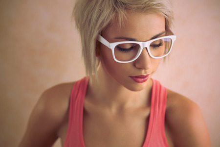 Beautiful young blond girl with short hair wearing glasses in pink styleの写真素材