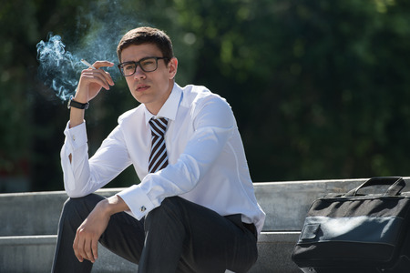 Well dressed business man smoking sitting on a street sidewalkの写真素材