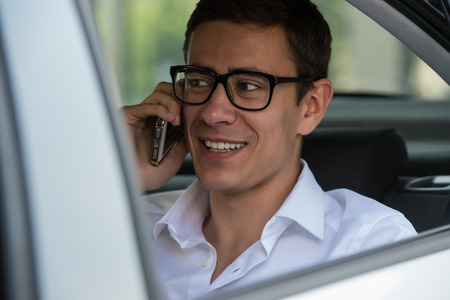 Happy young businessman using mobile phone in back seat of car