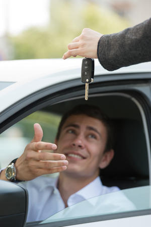 Car salesman handing over the keys for a new car to a young businessmanの写真素材