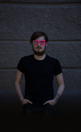 Stylish hipster model with dark hair and beard wearing pink glasses lifestyle in the street