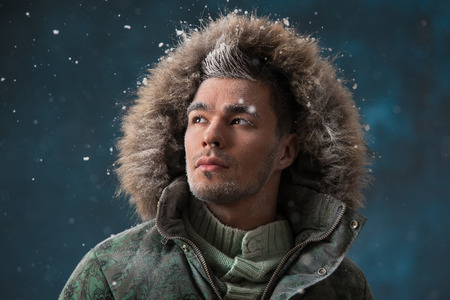 Handsome man wearing jacket with fur hood in winter snow at nightの写真素材