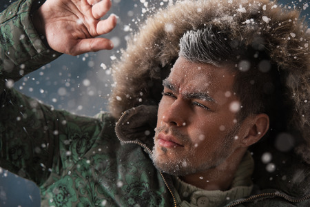 Handsome man wearing jacket with fur hood in winter snow at night