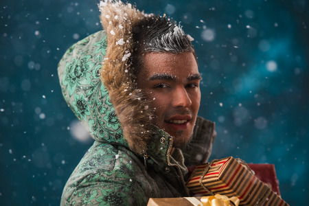 Handsome hispanic asian mixed ethnicity man carrying christmas gifts outdoors in winter under snowfallの写真素材
