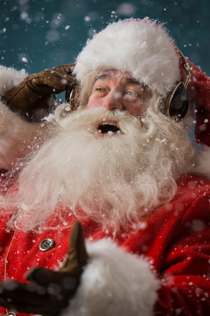 Santa Claus is listening to music in headphones outdoors at North Pole, Having fun while delivering giftsの写真素材