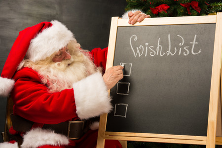 Santa Claus sitting near chalkboard with wishlist sign and blank copy space for checkboxes and your textの写真素材