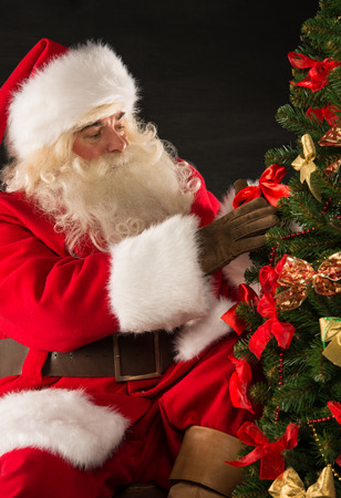 Santa Claus decorating Christmas tree in dark room の写真素材