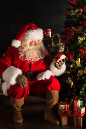 Santa putting gifts under Christmas tree in dark roomの写真素材