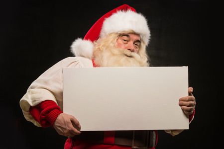 Santa Claus holding white blank sign with fun and smile standing against dark backgroundの写真素材